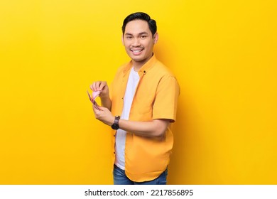 Smiling Young Handsome Asian Man Counting Money Banknotes Isolated On Yellow Background