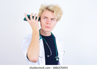Smiling young handsome Caucasian doctor man listening a voice message from her smartphone. Communication and technology concept.
