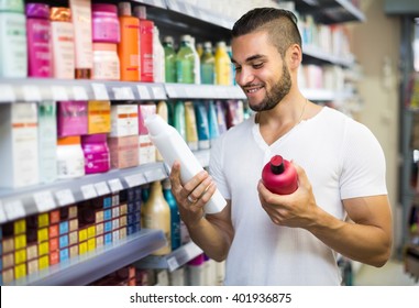 Smiling Young Handsome Man Selecting Shampoo In Supermarket
