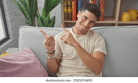 A smiling young hispanic man in a casual outfit points playfully while sitting on a sofa in a modern living room. - Powered by Shutterstock