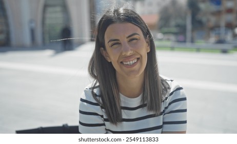 Smiling young hispanic woman with brunette hair in a striped shirt outdoors on a sunny urban street. - Powered by Shutterstock