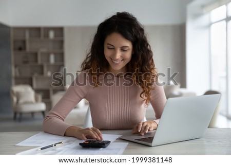 Smiling young Hispanic woman manage household family budget pay bills taxes on laptop online. Happy Latino female calculate expenditures expenses on machine, take care of finances or savings. ストックフォト © 