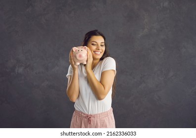 Smiling young Hispanic woman on black studio background hold piggybank with money investment. Happy millennial Latino female excited about saving in piggy bank. Financial stability concept.