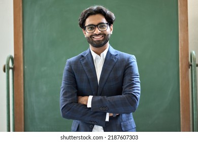 Smiling Young Indian Business Man Professional Manager Wearing Suit Looking At Camera Standing Arms Crossed In Office. Arab Teacher Or Professor Posing For Portrait At Work Desk In Front Of