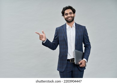 Smiling young indian business man, arab professional manager, eastern businessman executive wearing suit standing holding laptop pointing advertising isolated on beige background, portrait.