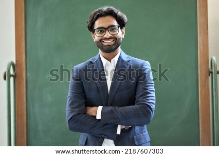 Smiling young indian business man professional manager wearing suit looking at camera standing arms crossed in office. Arab teacher or professor posing for portrait at work desk in front of ストックフォト © 