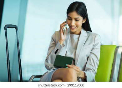 Smiling Young Indian Business Woman Talking On Mobile Phone While Waiting For Her Flight At Airport