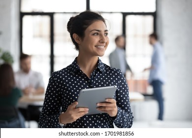 Smiling young Indian female employee hold tablet look in distance thinking, happy millennial biracial woman worker distracted from pad gadget, lost in thoughts visualizing, business vision concept