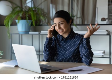 Smiling young Indian female employee consult client or customer online on smartphone work on computer. Happy ethnic businesswoman multitask in office use cellphone and laptop. Technology concept. - Powered by Shutterstock