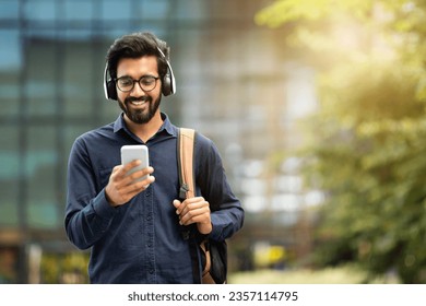 Smiling young indian man wearing wireless headphones holding phone having video call. Eastern businessman using smartphone, listening music in app tech on cellphone watching videos online, copy space - Powered by Shutterstock