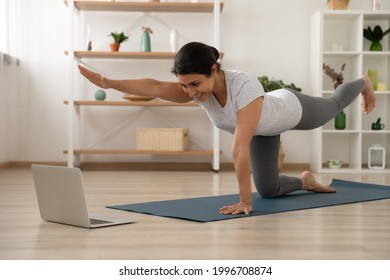 Smiling Young Indian Woman Do Morning Exercises Talk Speak On Video Webcam Call With Trainer Or Coach On Computer. Happy Ethnic Female Train Practice Yoga Watch Online Class On Laptop At Home.