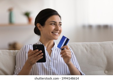 Smiling young Indian woman make online payment purchase on cellphone with bank credit debit card. Happy millennial mixed race female shopping on internet on smartphone from home. Technology concept.