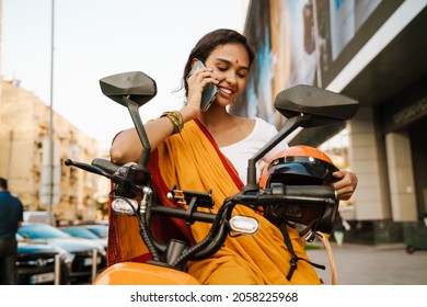 Smiling Young Indian Woman In Traditional Clothes Sitting On Scooter Talking On Mobile Phone On The Street