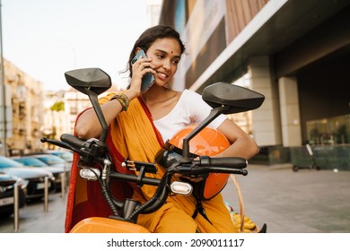 Smiling Young Indian Woman In Traditional Clothes Sitting On Scooter Talking On Mobile Phone On The Street