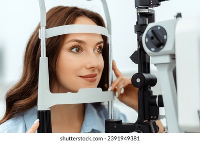 Smiling young lady examining her eyes with slit lamp in optical store. Medical examination