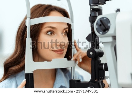 Smiling young lady examining her eyes with slit lamp in optical store. Medical examination