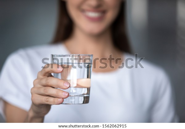 Smiling young lady holding fresh transparent pure\
filtered mineral water, happy healthy adult woman offering glass to\
camera as health care thirst hydration natural nutrition concept,\
close up view