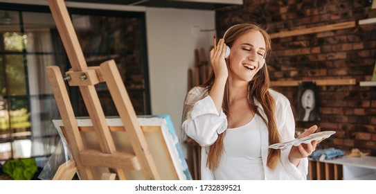 Smiling Young Lady Listening To Music And Painting Picture, Enjoying Art Therapy