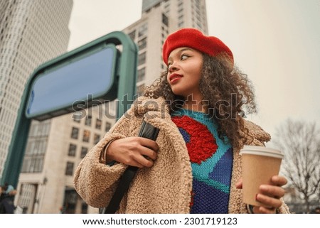 Smiling young lady is standing outside with cup of coffee