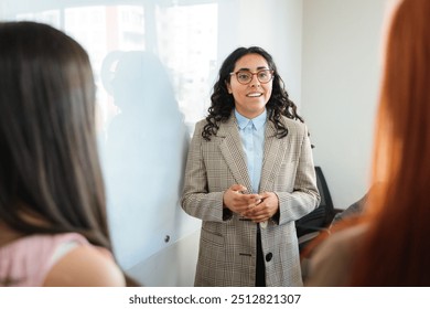 Smiling young latin businesswoman sharing business ideas with colleagues during a meeting on the whiteboard at office - Powered by Shutterstock