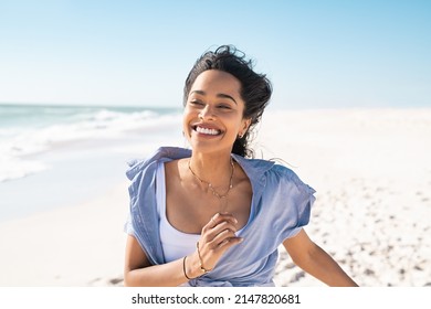Smiling young latin woman running on beach with a big grin. Mixed race girl enjoying vacation while running on beach. Carefree hispanic woman having fun at sea in summer. - Shutterstock ID 2147820681