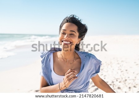 Smiling young latin woman running on beach with a big grin. Mixed race girl enjoying vacation while running on beach. Carefree hispanic woman having fun at sea in summer.