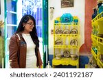 Smiling young Latin woman tourist wearing casual warm jacket and eyeglasses standing in Blue House of Frida Kahlo Museum in Mexico City and looking at exhibition