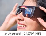 Smiling young latin woman watching an eclipse of the sun with eclipse glasses