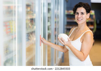 Smiling Young Latina Choosing Fresh Organic Dairy Products In Fridge At Grocery Store..