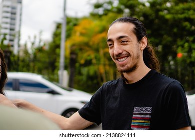 Smiling Young Latino Man With Long Hair Talking With His Friends