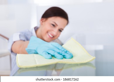 Smiling Young Maid Cleaning Glass Table At Home