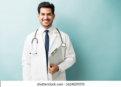 Smiling Young Male Doctor Holding Clipboard While Standing Against Colored Background