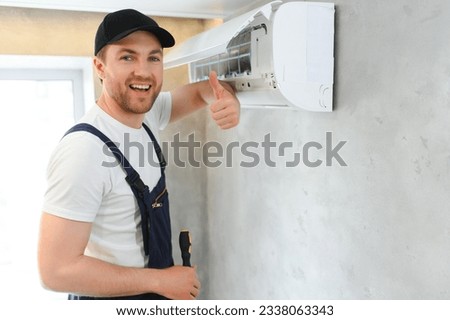 Smiling young male electrician repair conditioner in client home. Man mechanic or repairman fix filters in air condition device at customer house.