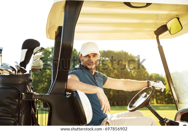 Smiling young male golfer sitting in a golf cart\
and looking at camera