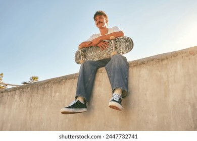 Smiling young male skateboarder holding skateboard sitting on ramp in skate park - Powered by Shutterstock