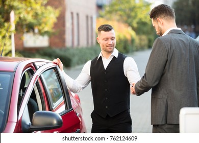 Smiling Young Male Valet And Businessperson Standing Near Red Car