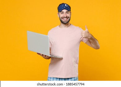 Smiling Young Man 20s In Pajamas Home Wear Sleep Mask Working On Laptop Pc Computer Showing Thumb Up Resting At Home Isolated On Yellow Background Studio Portrait. Relax Good Mood Lifestyle Concept