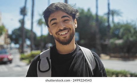 Smiling young man with beard and backpack standing on a sunny urban street lined with palm trees - Powered by Shutterstock