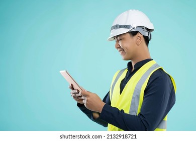 Smiling young man building engineer in helmet using tablet,green background