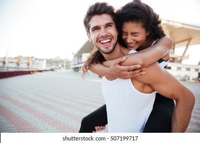 Smiling young man carrying woman on his back and laughing outdoors - Shutterstock ID 507199717