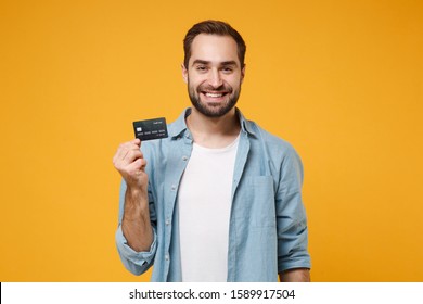 Smiling Young Man In Casual Blue Shirt Posing Isolated On Yellow Orange Wall Background, Studio Portrait. People Sincere Emotions Lifestyle Concept. Mock Up Copy Space. Hold In Hand Credit Bank Card