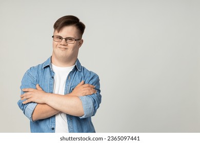A smiling young man with cerebral palsy in glasses, jeans and a white T-shirt poses for the camera. World Genetic Diseases Day concept, place for text