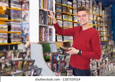 Smiling Young Man Choosing Movies On DVD From Large Assortment At Store