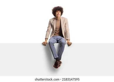 Smiling young man with curly hair sitting on a blank panel isolated on white background - Powered by Shutterstock