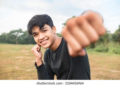 A smiling young man in a dark gray sweatshirt doing shadow boxing outside a field. Throwing a right jab towards the camera. - Powered by Shutterstock