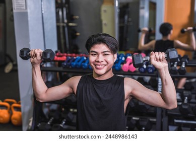 A smiling young man does a set of seated dumbbell shoulder presses. A slim teenager building muscle at the gym. - Powered by Shutterstock