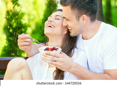 Smiling young man feeding his loving woman on a sunny morning in their garden.