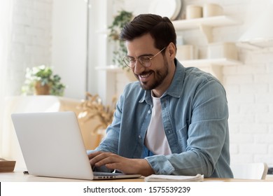 Smiling young man freelancer using laptop studying online working from home, happy casual millennial guy typing on pc notebook surfing internet looking at screen enjoying distant job sit at table