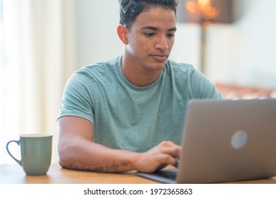 Smiling young man freelancer using laptop studying online working from home, happy casual hipster guy typing on pc notebook surfing internet looking at screen enjoying distant job sit at table