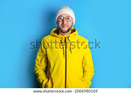 Smiling young man with glasses in a yellow jacket on a blue background.